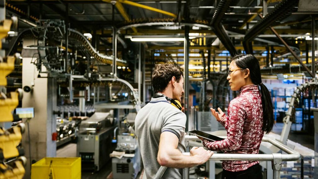Mechanic and manager talking nearby a machine in a big printery about latest newspaper print