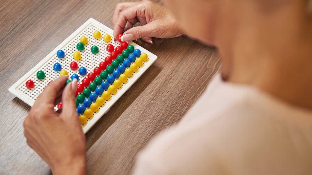 Person placing small colorful pegs onto a board for occupational therapy exercise.